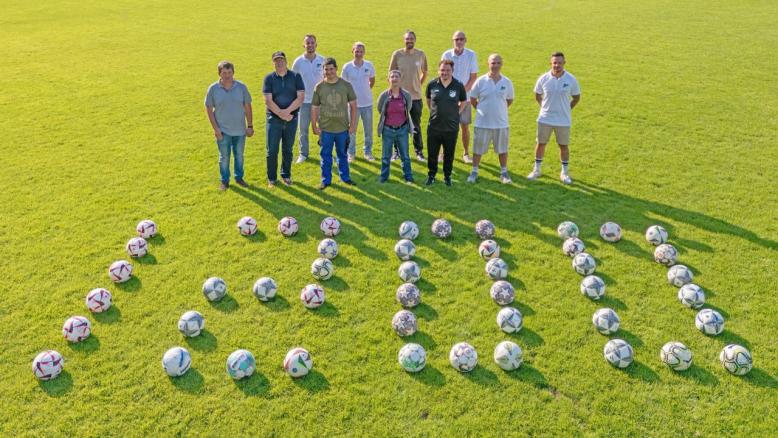 Personen von TUS und Club stehen auf dem Fussballfeld vor Fussbällen, die als Zahl 1.200 angeordnet sind.