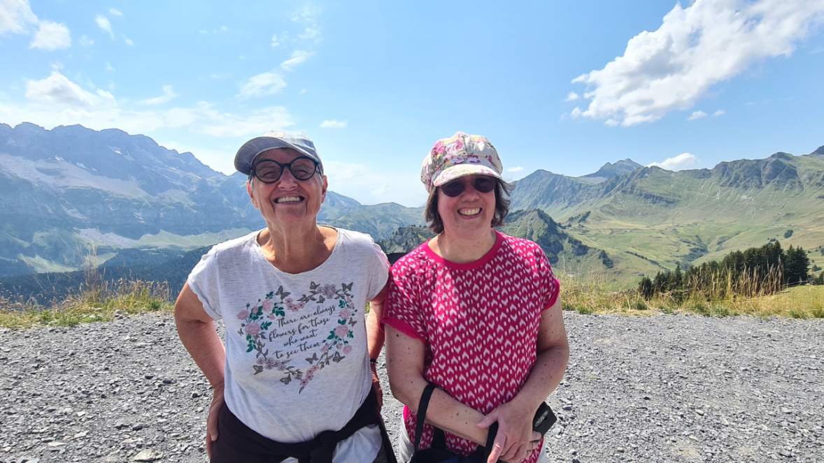 Zwei Frauen stehen vor einer Bergkette und lachen in die Kamera.
